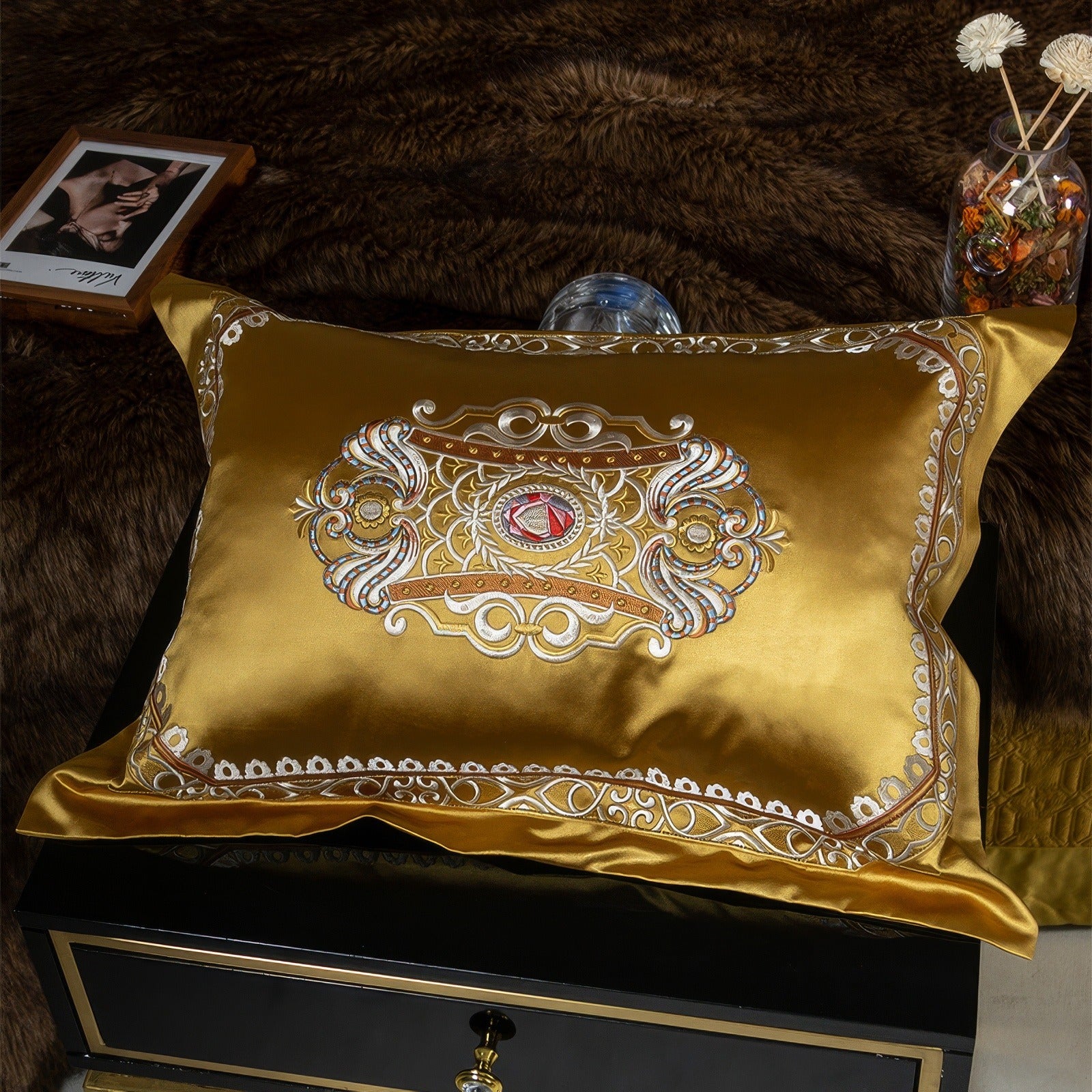 Gold satin pillowcase featuring intricate embroidery with a regal, symmetrical design in metallic hues of silver and red accents, set against a textured dark background for a luxurious and sophisticated aesthetic.

