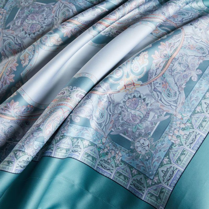 Close-up view of a silky turquoise fabric featuring intricate pastel designs and detailed patterns, showcasing the luxurious texture and artistry of the material.

