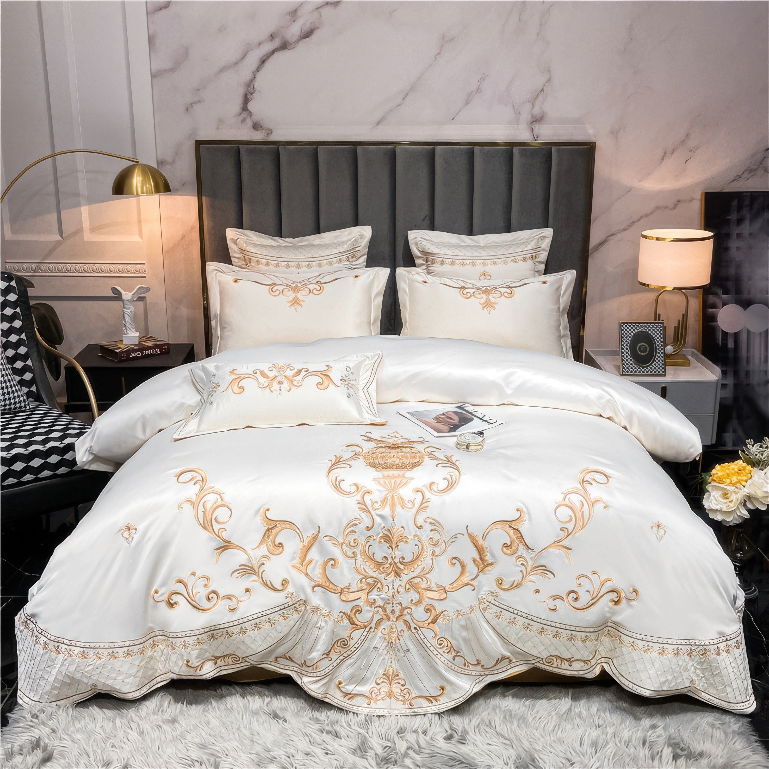 Egyptian cotton bedding in an ivory-white color with gold embroidery featuring intricate baroque-style patterns. The luxurious duvet set includes matching pillowcases with elegant detailing and a soft, lustrous finish, complementing the sophisticated bedroom décor. The plush grey rug contrasts with the bedding's rich texture, while soft ambient lighting adds to the opulent atmosphere.

