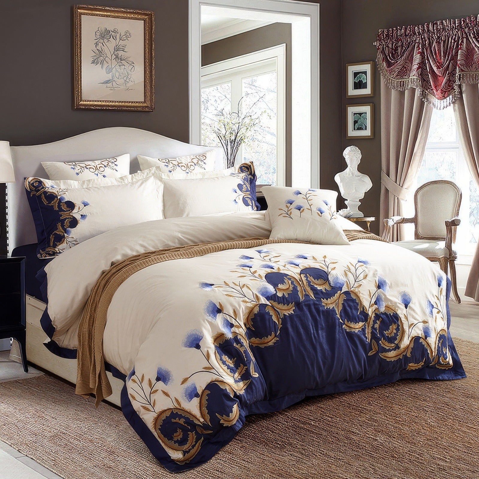 Egyptian cotton bedding set featuring elegant blue and gold floral embroidery on a white duvet cover with a rich navy-blue border. The set includes matching pillowcases and a decorative cushion, arranged on a bed with a white upholstered headboard in a classic, well-lit bedroom. The luxurious Egyptian cotton fabric enhances the bedding's softness, durability, and premium quality.

