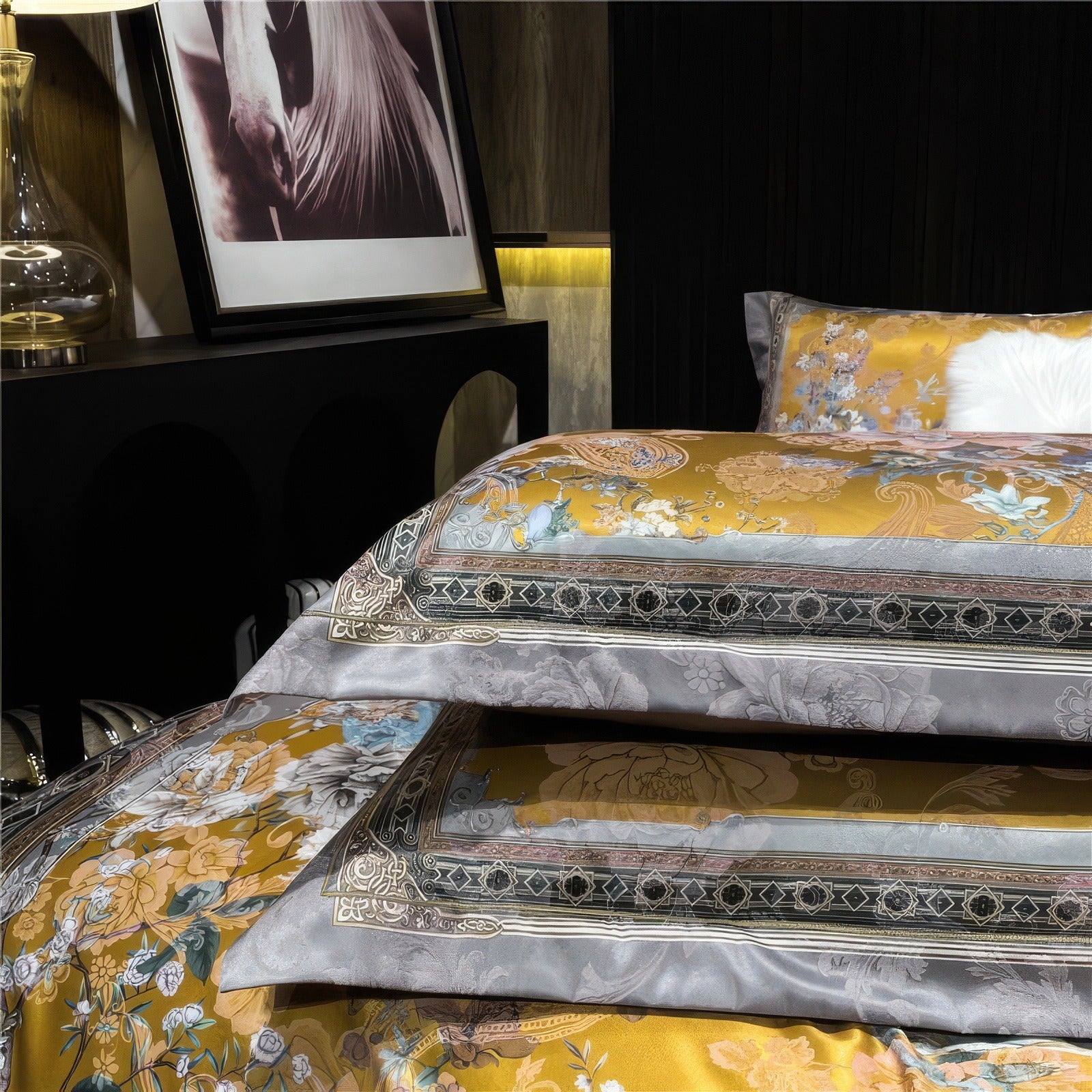 Stacked pillows with golden floral and intricate gray patterns, set against a matching luxurious bedding ensemble with a bold design and silky finish.

