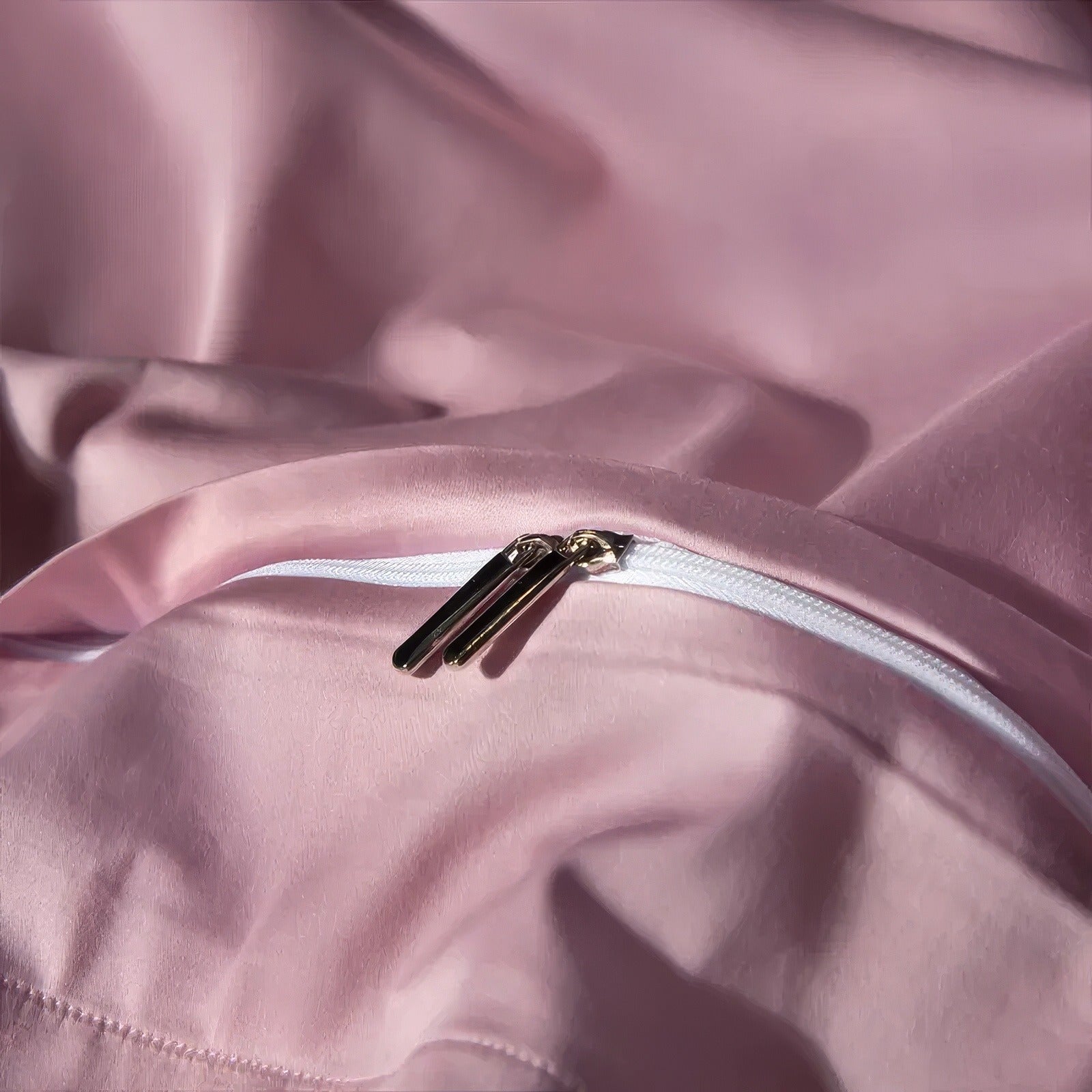 Close-up of a pink duvet cover showcasing a white zipper with two gold zipper pulls against the smooth fabric.

