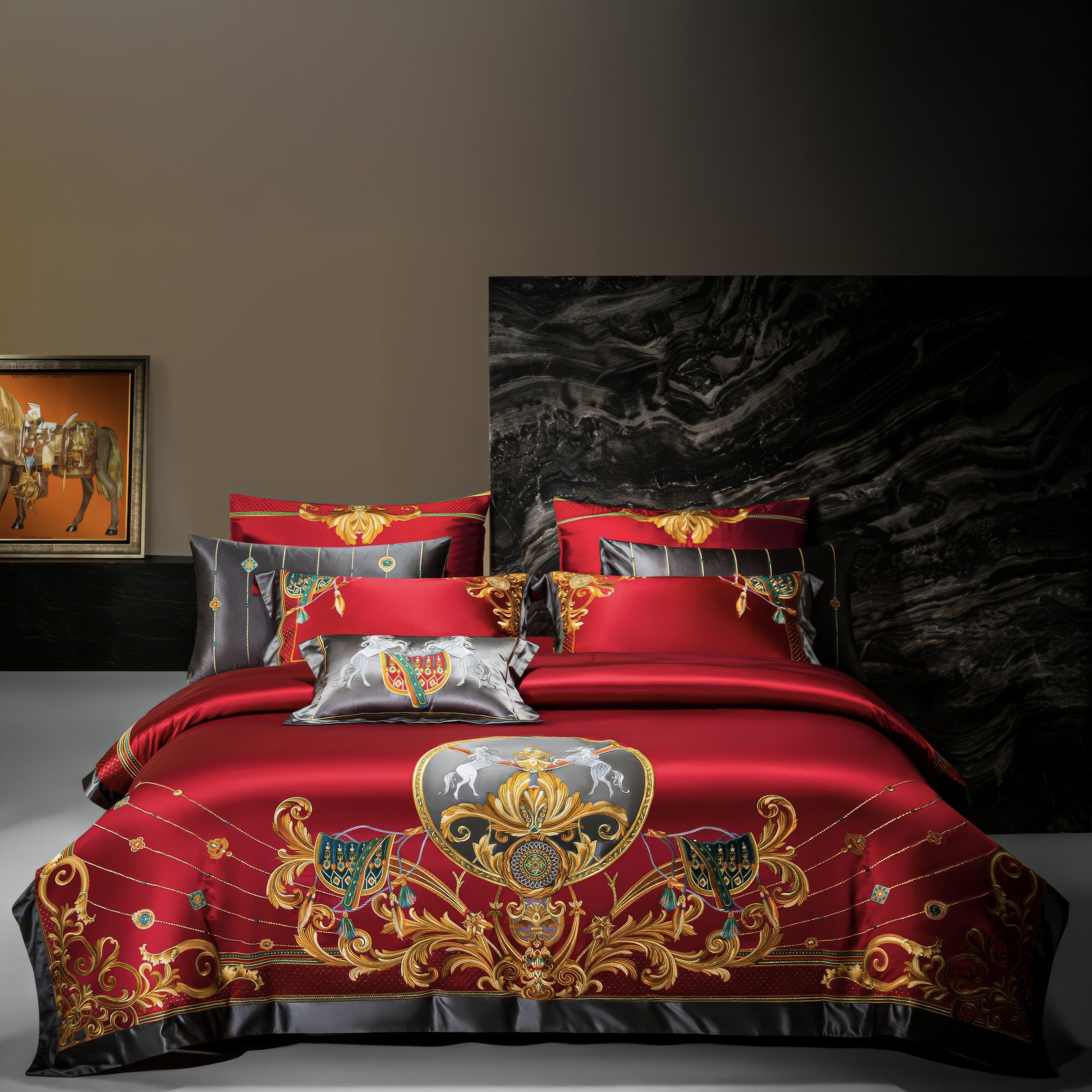 A luxurious bedding set in a bold red satin, adorned with intricate golden and black embroidery featuring regal motifs such as rearing horses and ornate shields. The centerpiece design is complemented by coordinating pillowcases with matching patterns. A black marble headboard serves as a dramatic backdrop, enhancing the vibrant red and gold color scheme. A framed equestrian painting on the side wall adds a touch of classical elegance, completing the opulent and royal aesthetic of the room.