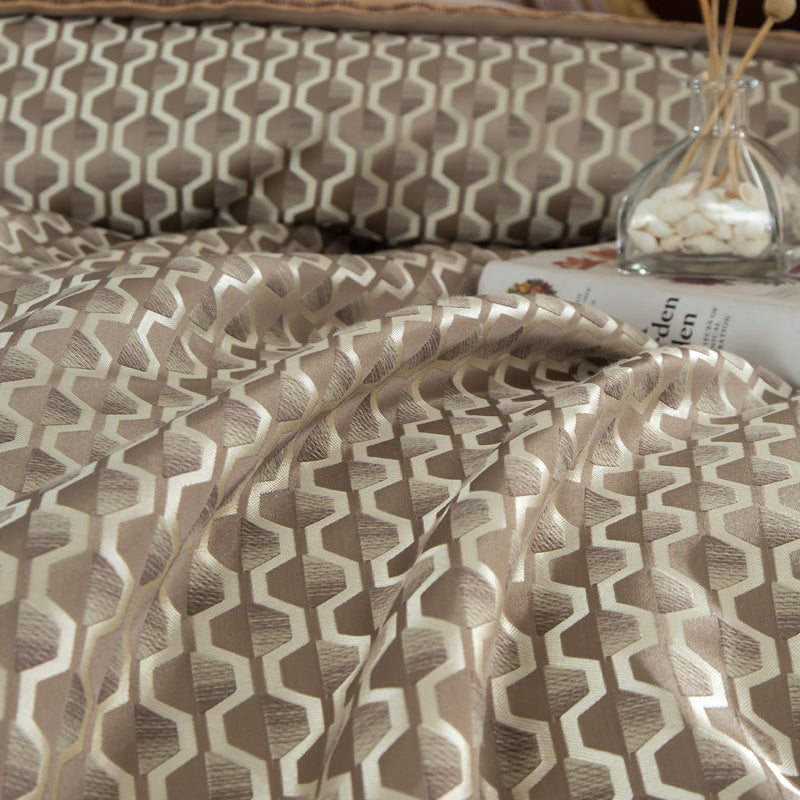 An elegant close-up of a beige and brown bedding design, showcasing a hexagonal geometric pattern complemented by a luxurious satin border adorned with intricate gold embroidery. The addition of a brass hourglass enhances the refined and timeless aesthetic.



