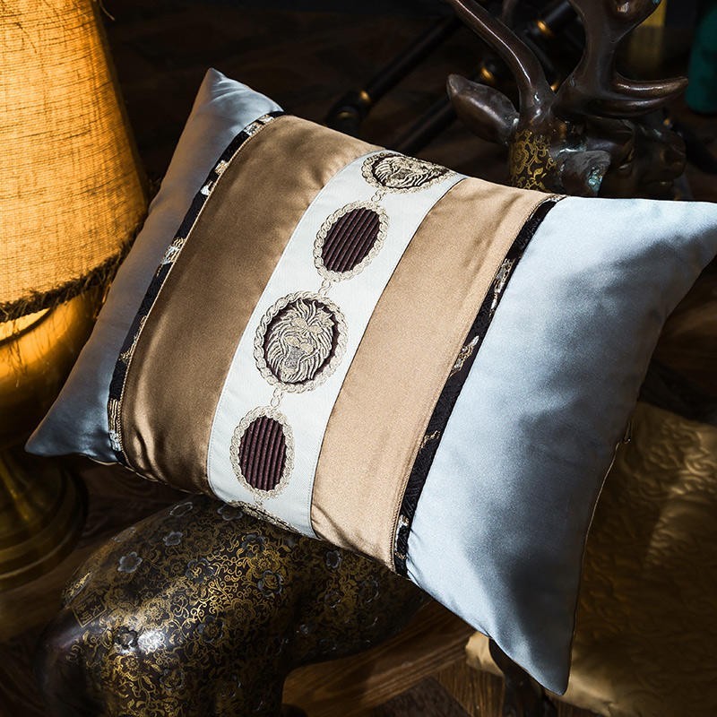 A decorative pillow crafted from Egyptian cotton, featuring an opulent design. The pillow combines pale blue and bronze panels, highlighted by an embroidered center strip with intricate circular motifs in gold and maroon tones. Black and gold trim frames the edges, adding a touch of elegance. The smooth, lustrous finish of the Egyptian cotton enhances the luxurious appeal.

